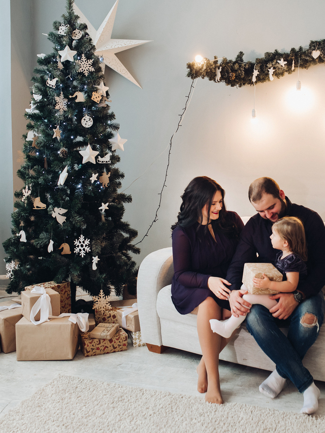 Young caucasian family of three sit on the sofa next to the Christmas tree together