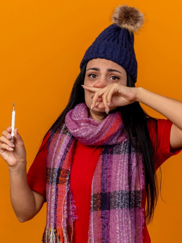 fraca-e-jovem-caucasiana-doente-com-chapeu-de-inverno-e-lenco-segurando-um-termometro-e-limpando-o-nariz-isolado-na-parede-laranja_141793-79725