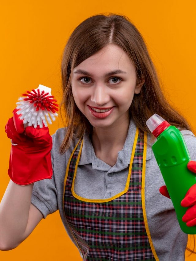 menina-linda-de-avental-e-luvas-de-borracha-segurando-material-de-limpeza-e-escova-de-esfregar-sorrindo-alegremente-olhando-para-a-camera-com-astucia_141793-28459