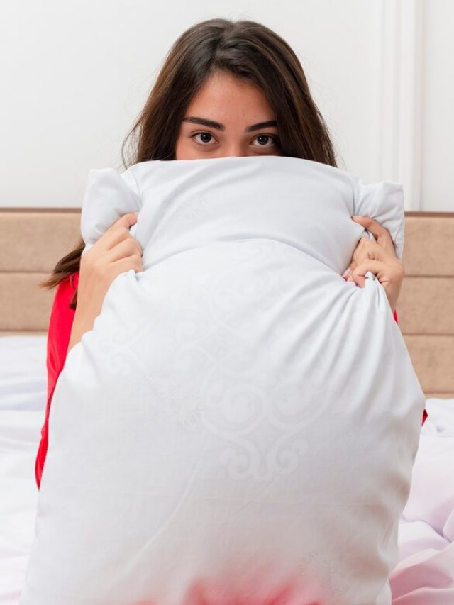 jovem-mulher-bonita-de-pijama-vermelho-sentada-na-cama-com-uma-almofada-escondida-atras-dela-no-interior-do-quarto_141793-102490