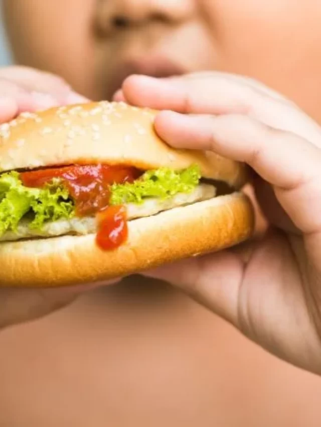 crianca-com-disturbio-de-obesidade-infantil-segurando-hamburguer-com-as-duas-maos-e-o-levando-a-boca.jpg