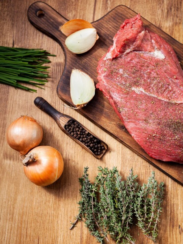 carne-crua-do-acougue-na-placa-de-madeira-com-ingredientes-cebola-crua-ervas-verdes_482257-19697